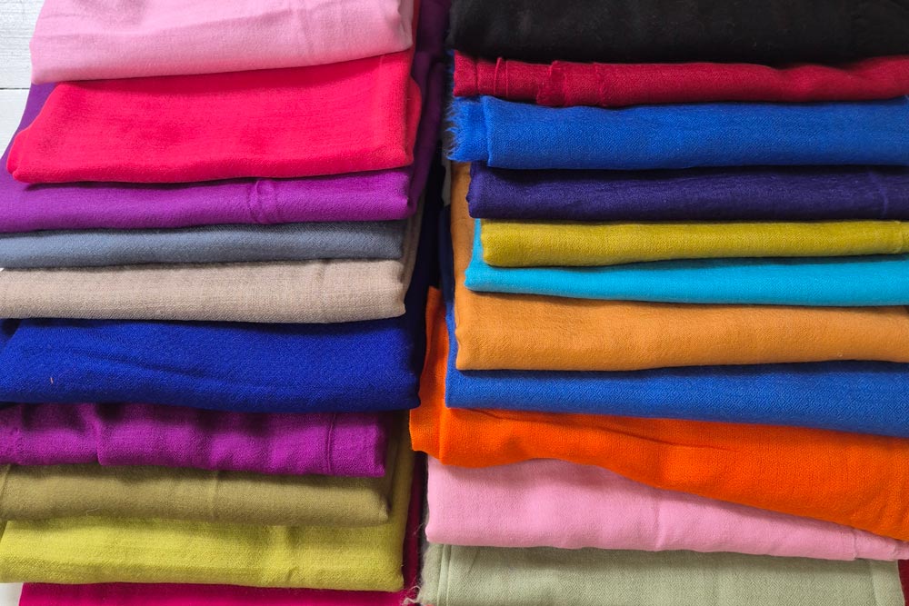 Flera kashmir sjalar i olika färger vikta i en hög