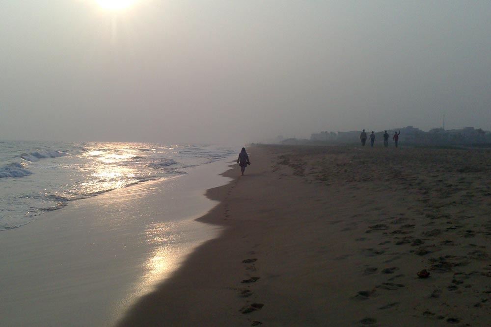 Person som går längs en sandstrand i Indien